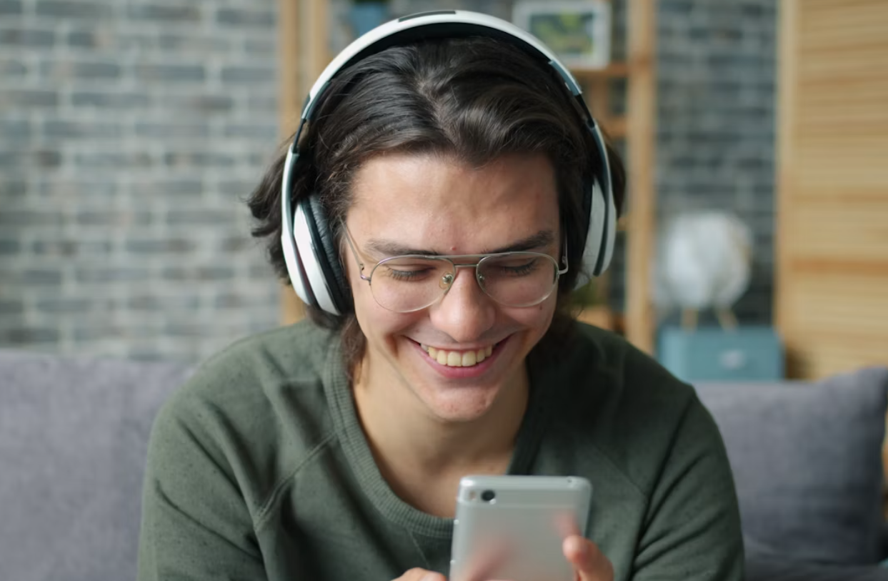 Mand sidder på sofa og kigger på sin telefon med høretelefoner på. Han smiler fordi han har fået nyt udstyr.