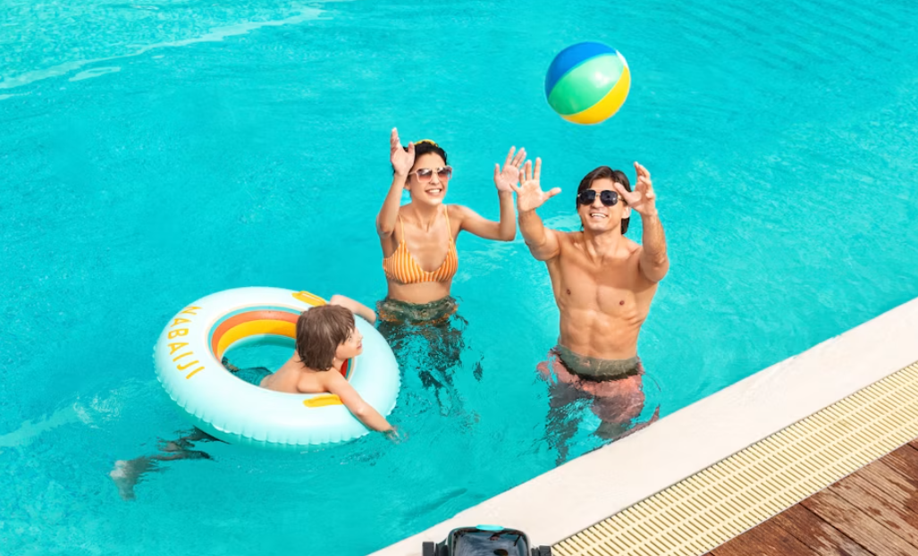 Familie i pool. Mor og far kaster med en badebold mens barnet flyder rundt med en badering.